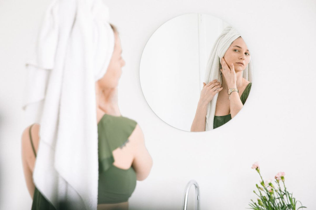 Vrouw bekijkt haar acnegevoelige huid in de spiegel en twijfelt over haar skincare routine.
